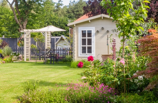 English garden in summer with summerhouse with trees, plants and flowers.